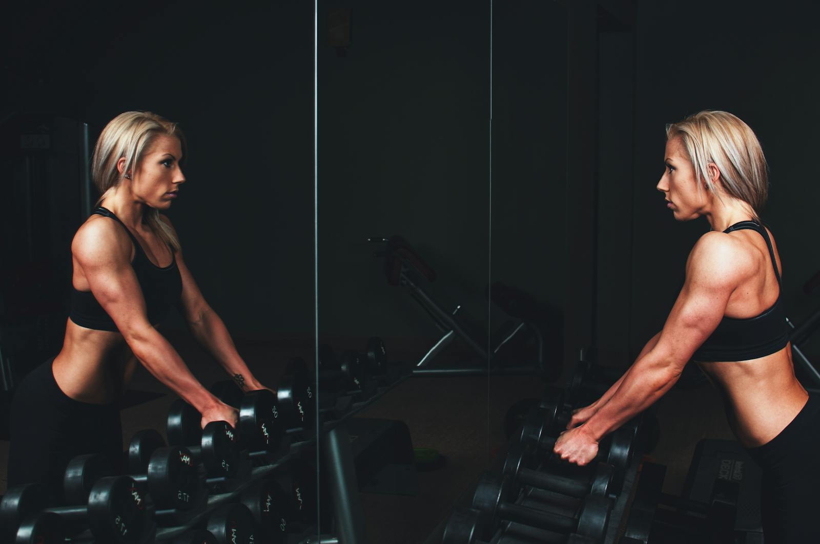 Athletic woman engaging in strength training exercise with dumbbells in a gym setting, reflecting on progress.